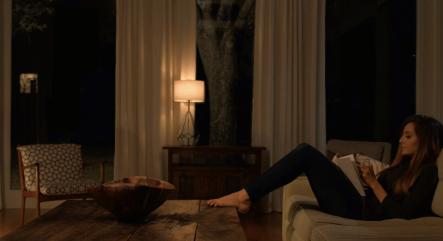 Woman sitting on a couch reading a book while propping her feet up on the coffee table.