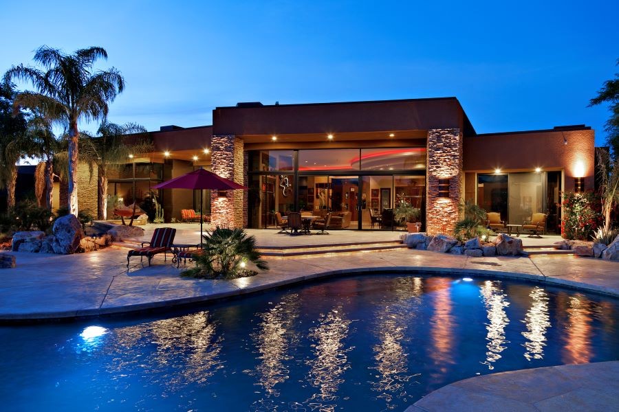 A home’s backyard at dusk with an illuminated pool, plants, and architectural features.